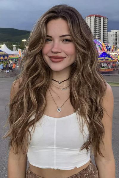 Een jonge vrouw met lang, golvend haar en middenscheiding, draagt een witte crop top en staat buiten op een festivalterrein.
