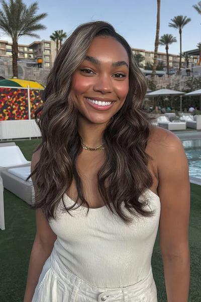 Een vrouw met lang golvend haar en subtiele highlights, gestyled in losse, natuurlijke krullen.