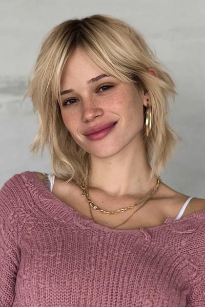 Een vrouw met een halflange, warrige blonde bob met lichte golven en een losse pony.