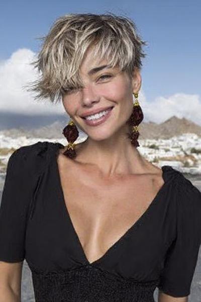 Een vrouw met een kort, warrig kapsel met blonde highlights en een zijscheiding, lachend buiten.